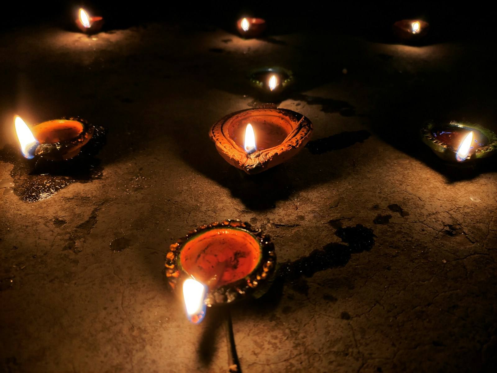 Lit clay diya lamps placed on a dark floor at night.